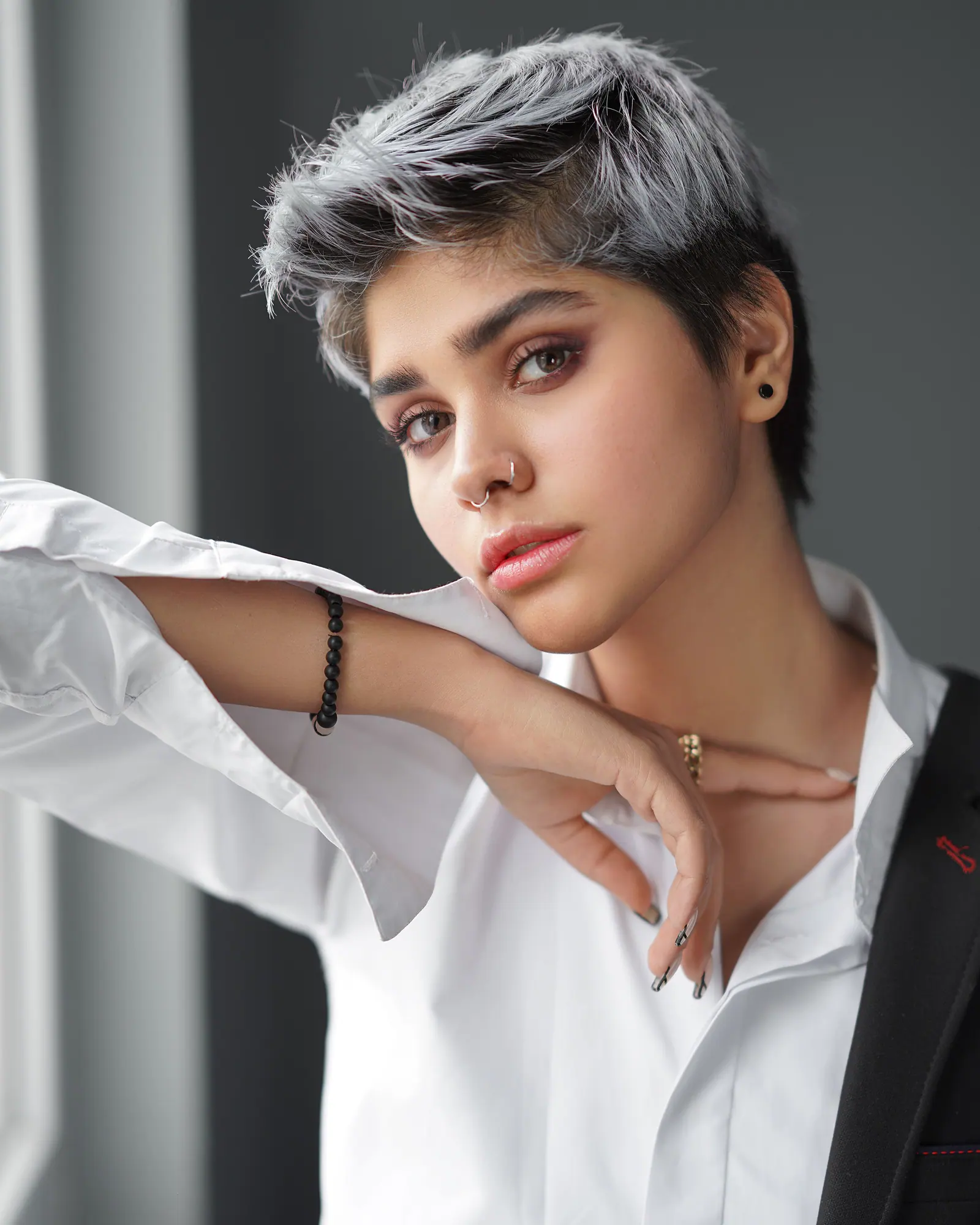Person with a silver-tipped pixie in a crisp white shirt resting their chin on their wrist