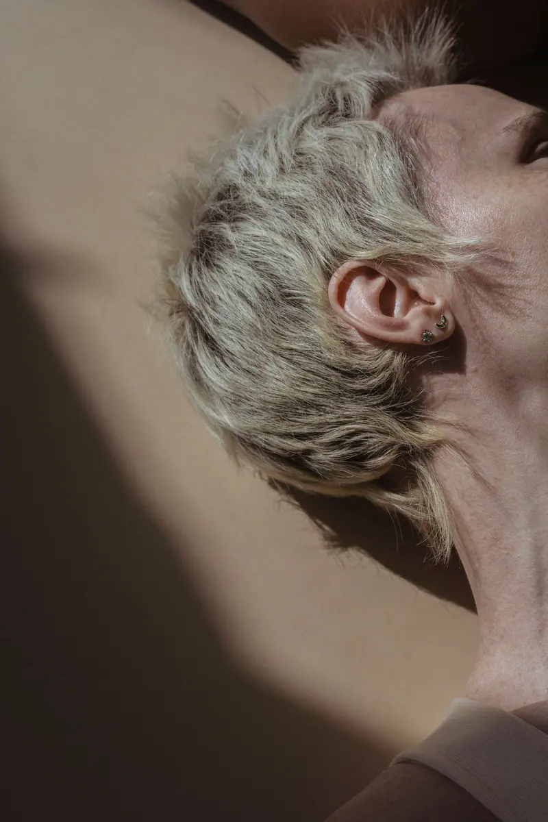 Close-up of a serene woman with short blond hair, lying in gentle, soft lighting indoors.