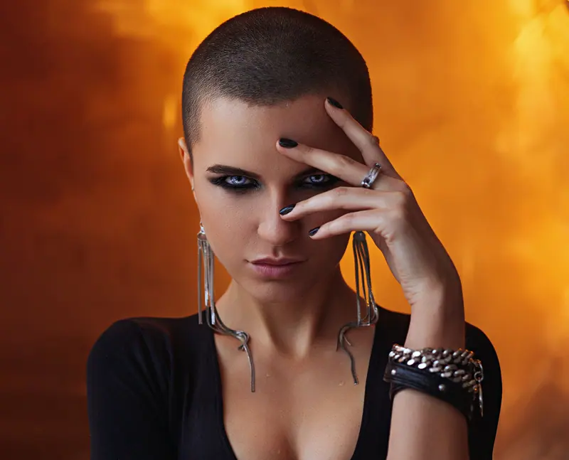 Striking portrait of a woman with shaved hair, bold makeup, and statement accessories.