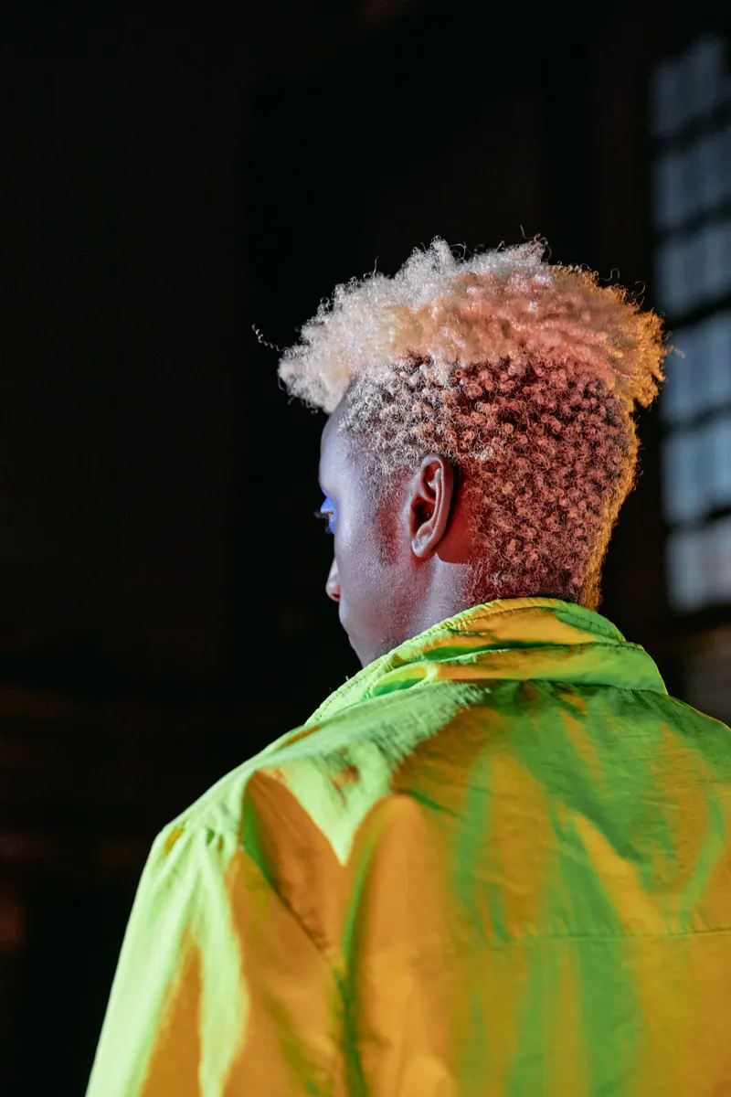 Back view of man with afro hair wearing a neon green jacket, shot indoors.