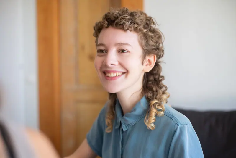 Smiling person with a curly mullet in a denim shirt