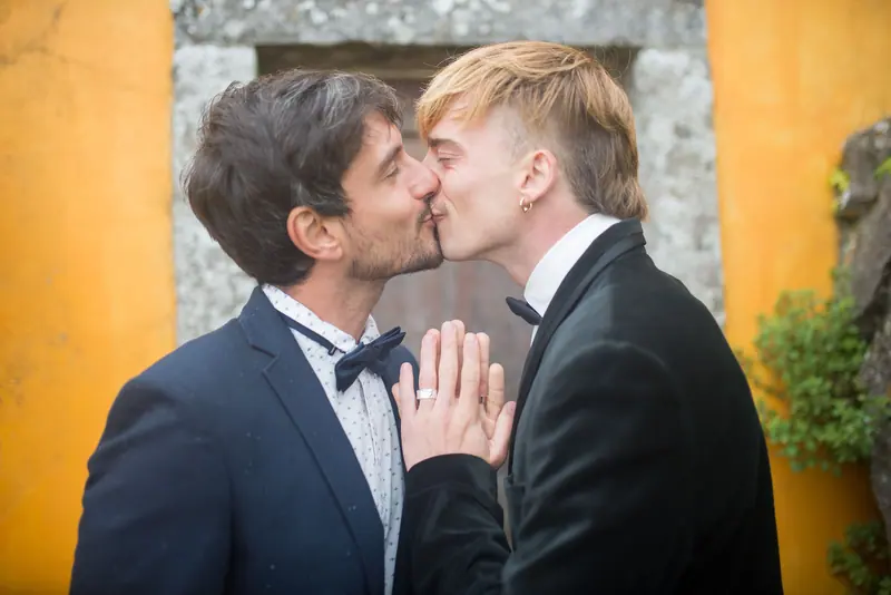 Two grooms kissing against a golden wall