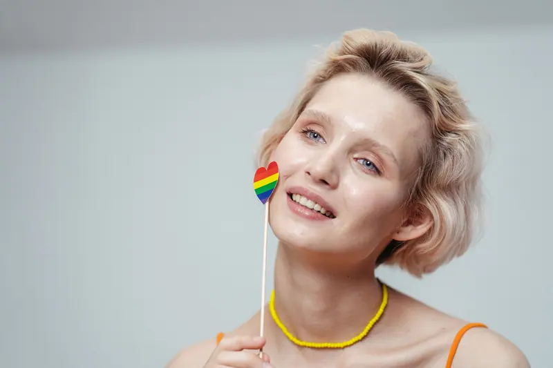 Woman with a short blonde bob holding a small rainbow heart