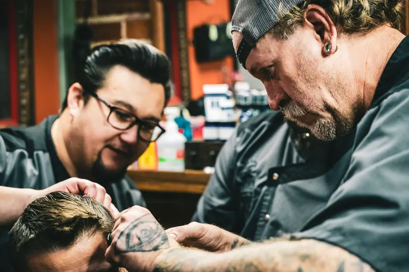 Two tattooed barbers working together on a client's cut