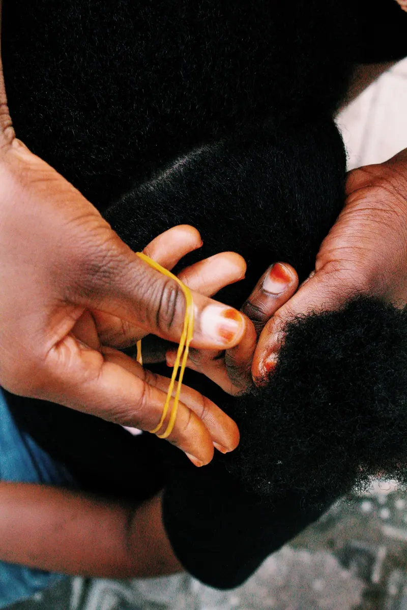 Close-up of a mother braiding her daughter's curly hair, showcasing cultural beauty and bond.