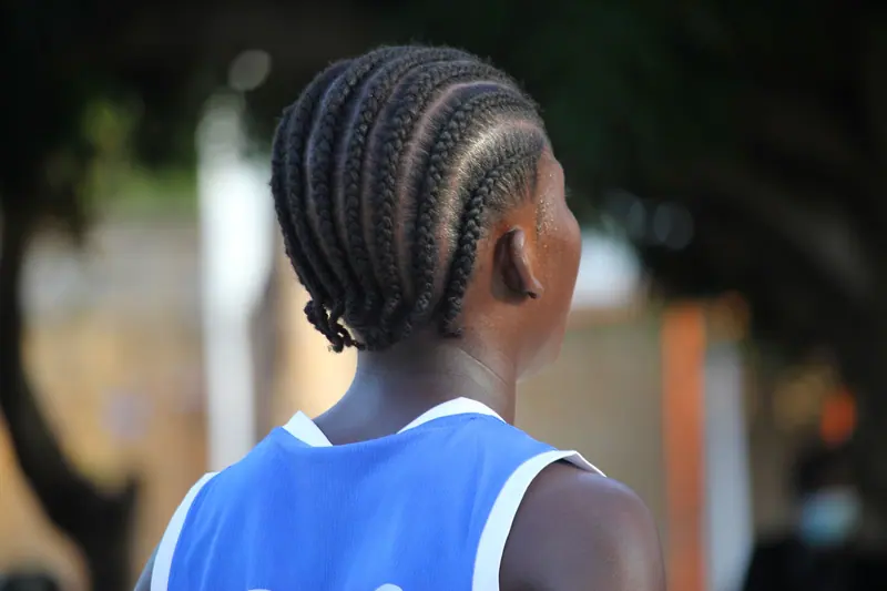 Back view of a person with cornrow braids in a blue jersey outdoors during the day.