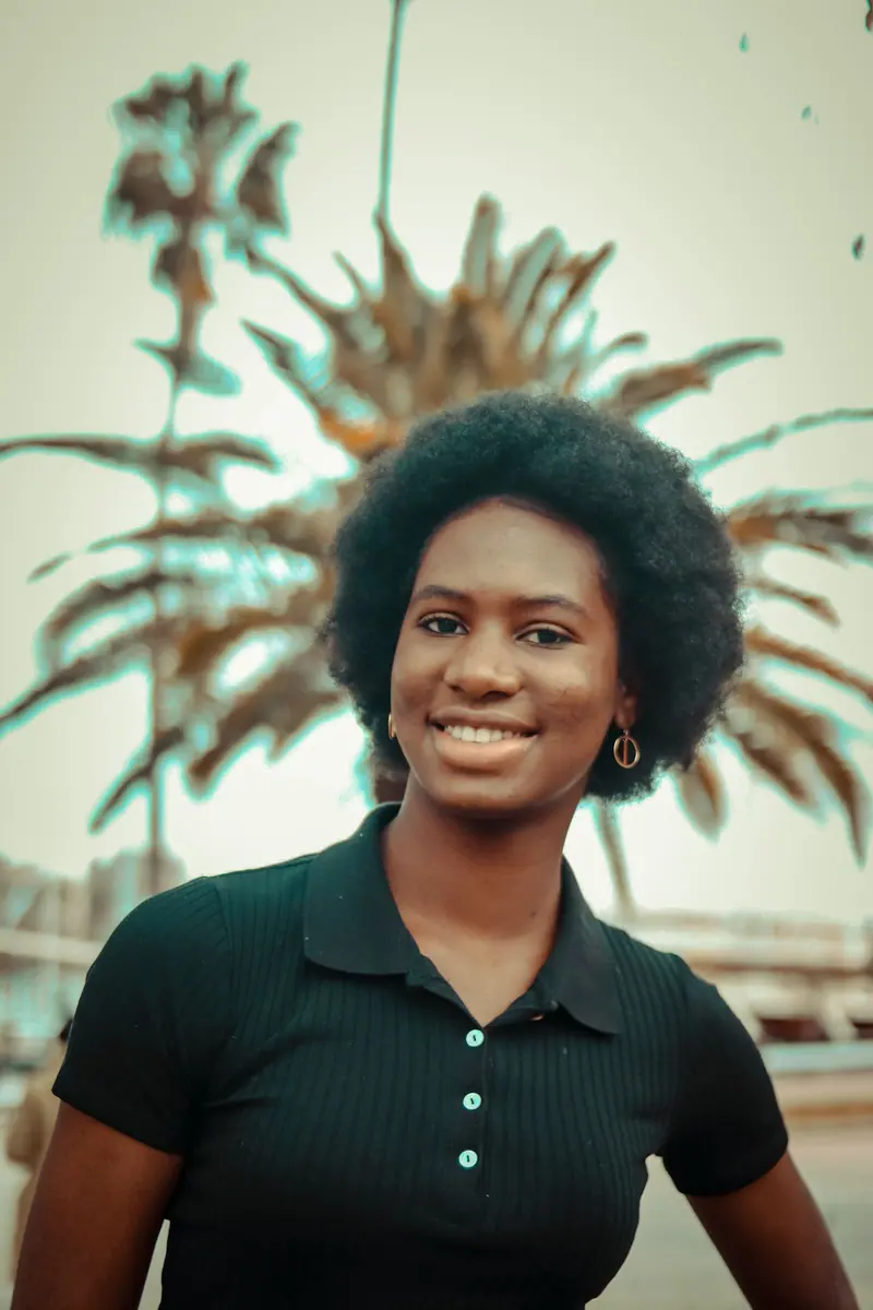Portrait of a cheerful woman with afro hair smiling outdoors against palm trees.