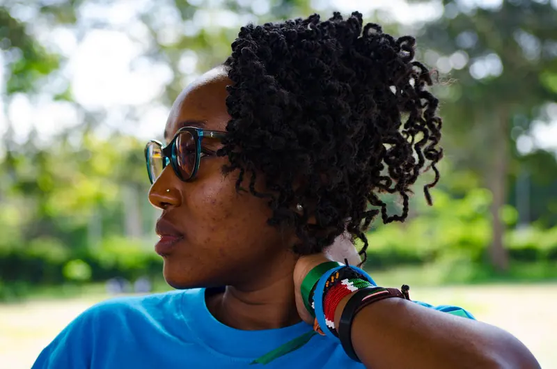 African woman with sunglasses and bracelets enjoying a sunny day outdoors.