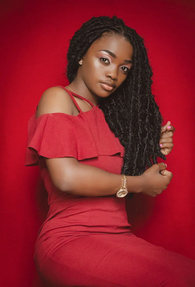 Woman with long locs in a red dress against a red wall