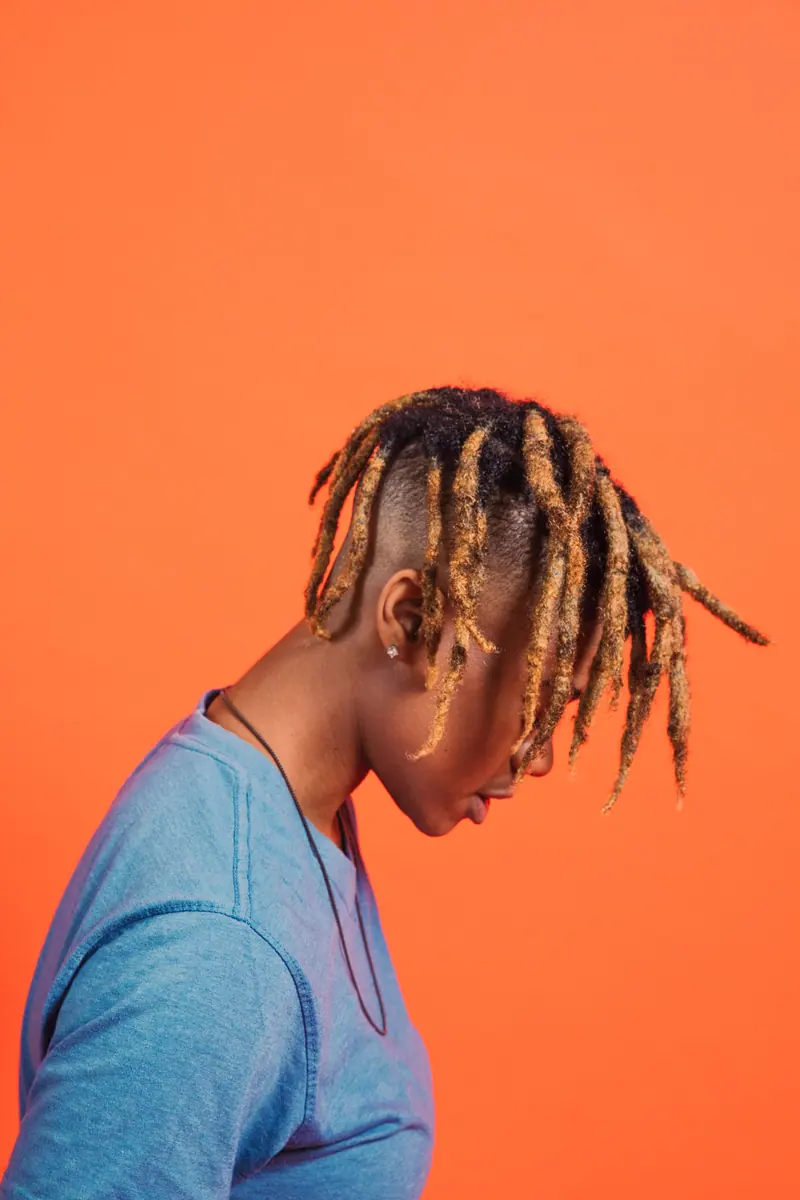 Side view portrait featuring dreadlocks against a vibrant orange backdrop, showcasing unique fashion style.