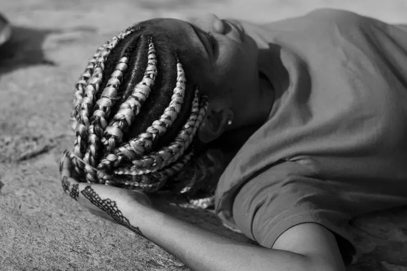 Artistic black and white photo of a woman with braided hair lying on the ground.