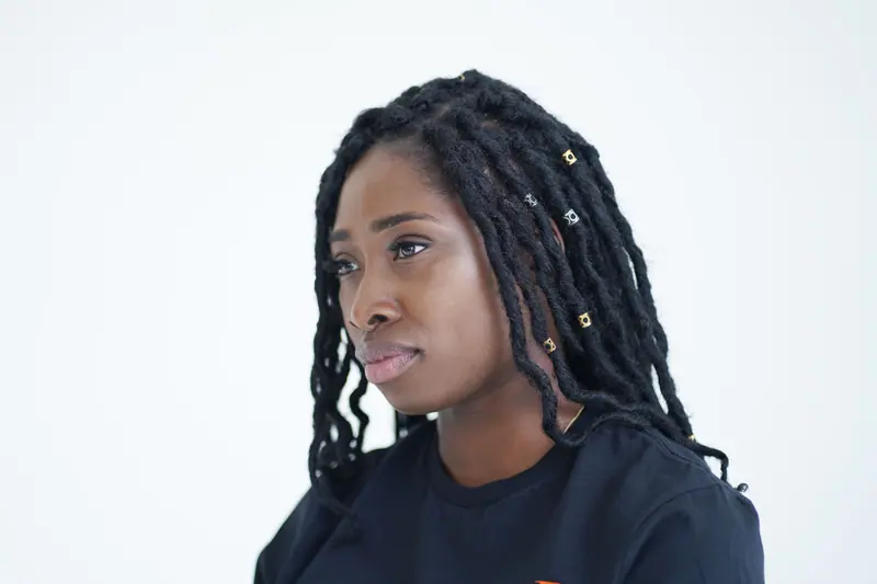 Headshot of a woman wearing a black top with dreadlocks and hair accessories.