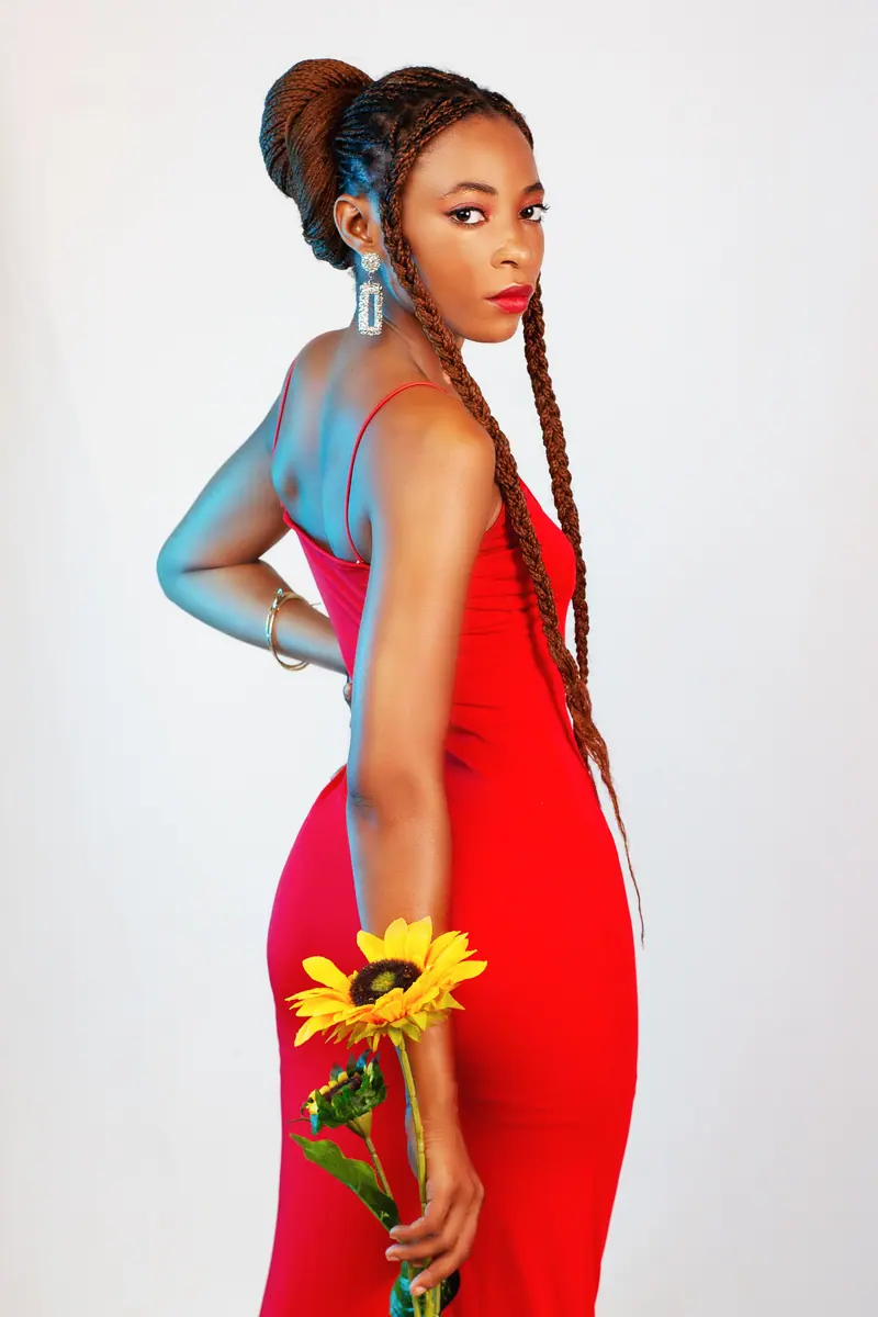 Stylish woman in a red dress holding a sunflower, posing elegantly in a studio shoot.