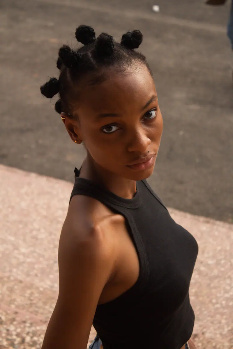 A striking portrait of a woman with Bantu knots in a sleeveless top, posing outdoors.