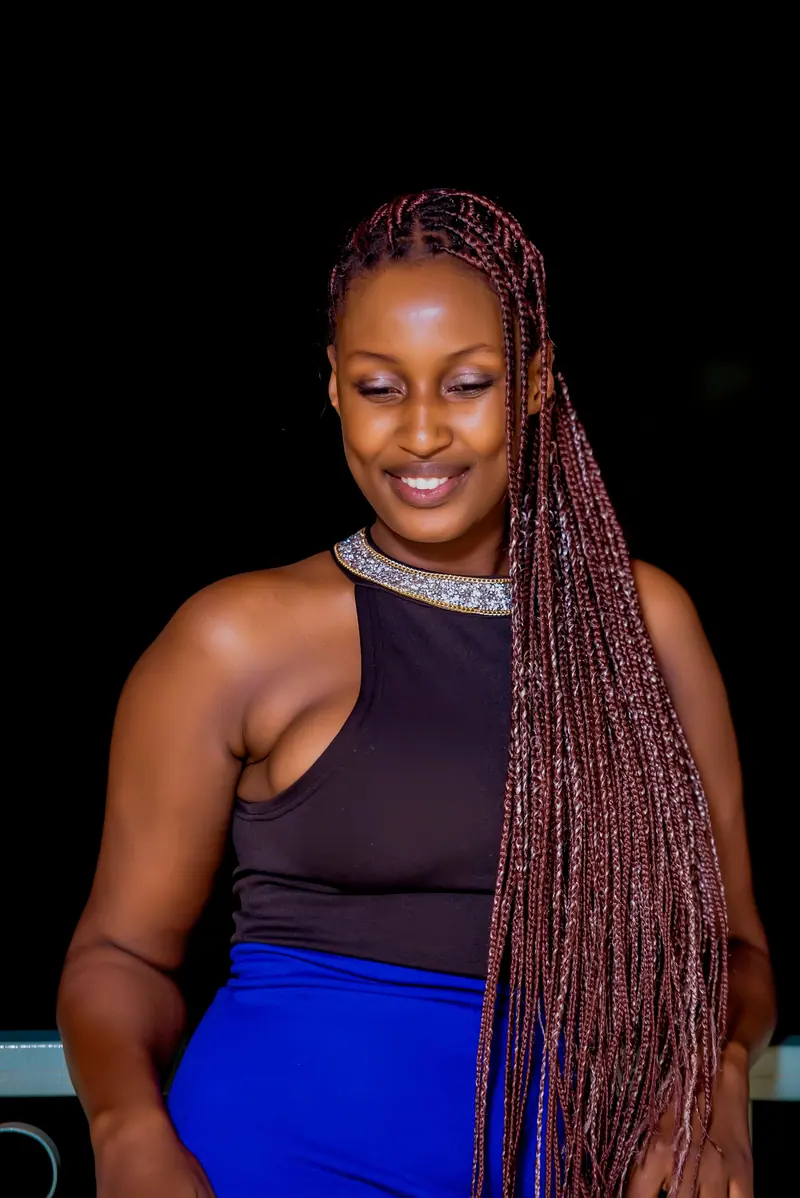 Portrait of a stylish young woman with long braided hair smiling against a dark background.