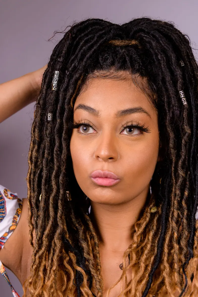 Close-up portrait of a black woman with long dreadlocks looking thoughtful. Vertical shot.