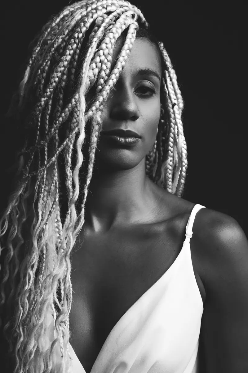 Striking black and white portrait of a woman with braided hair against a dark background.