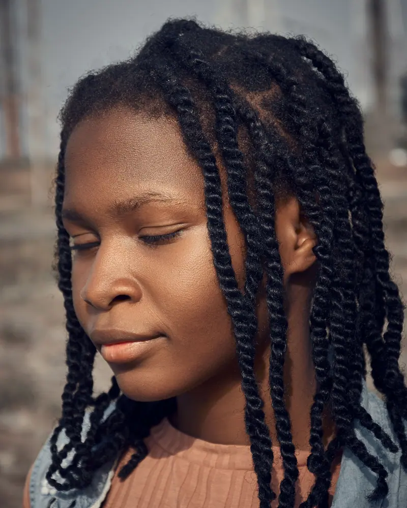 Close-up portrait of a young woman with braided hair enjoying a peaceful moment outdoors.