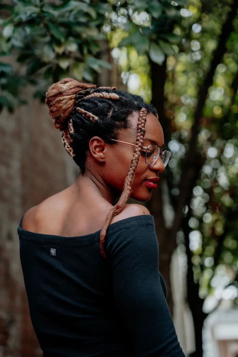 A woman with braided hair and glasses poses outdoors, showcasing stylish fashion.