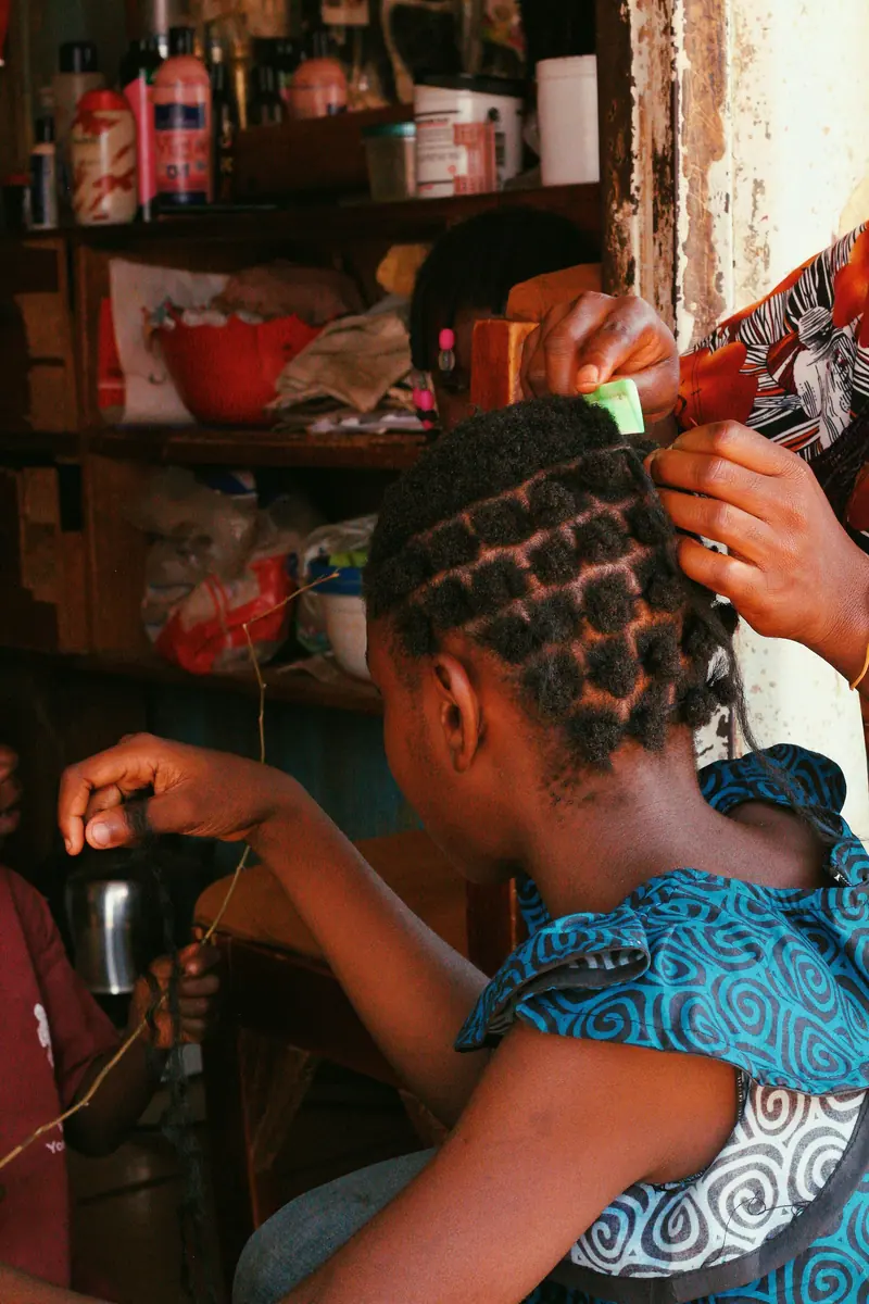 Girl getting intricate braids in a local Abuja salon. Captures cultural beauty.