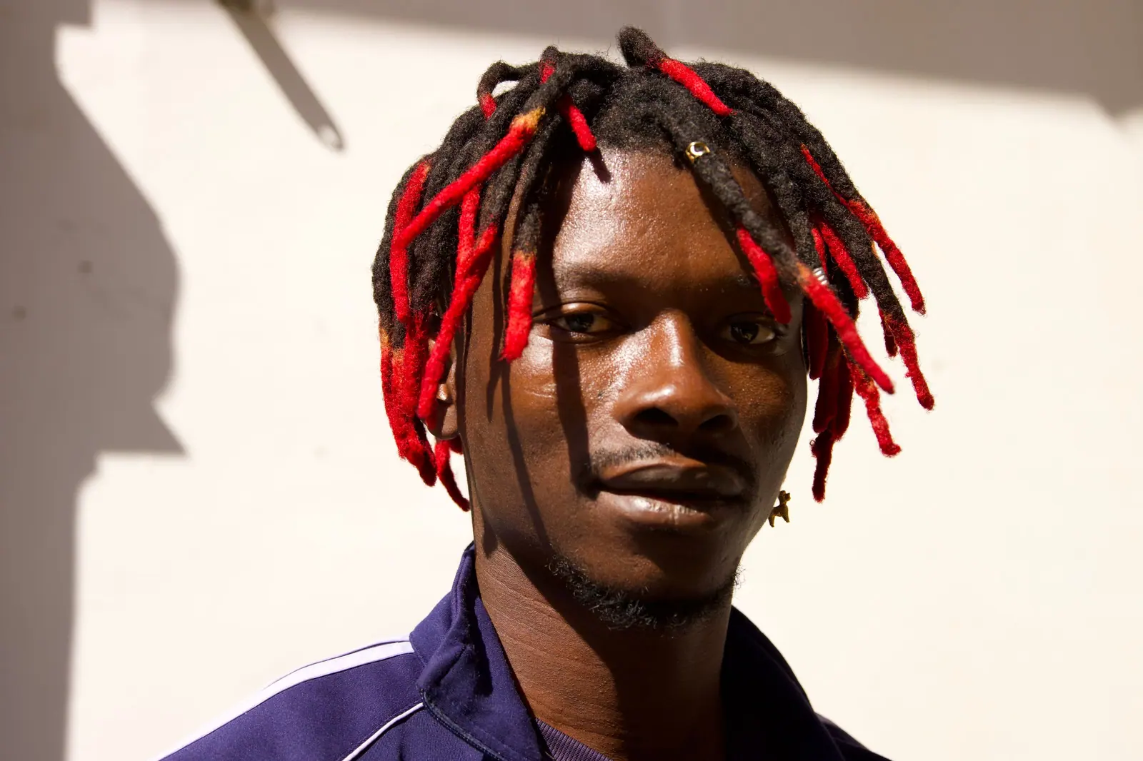 Man with red-dyed locs looking into the camera in warm sunlight