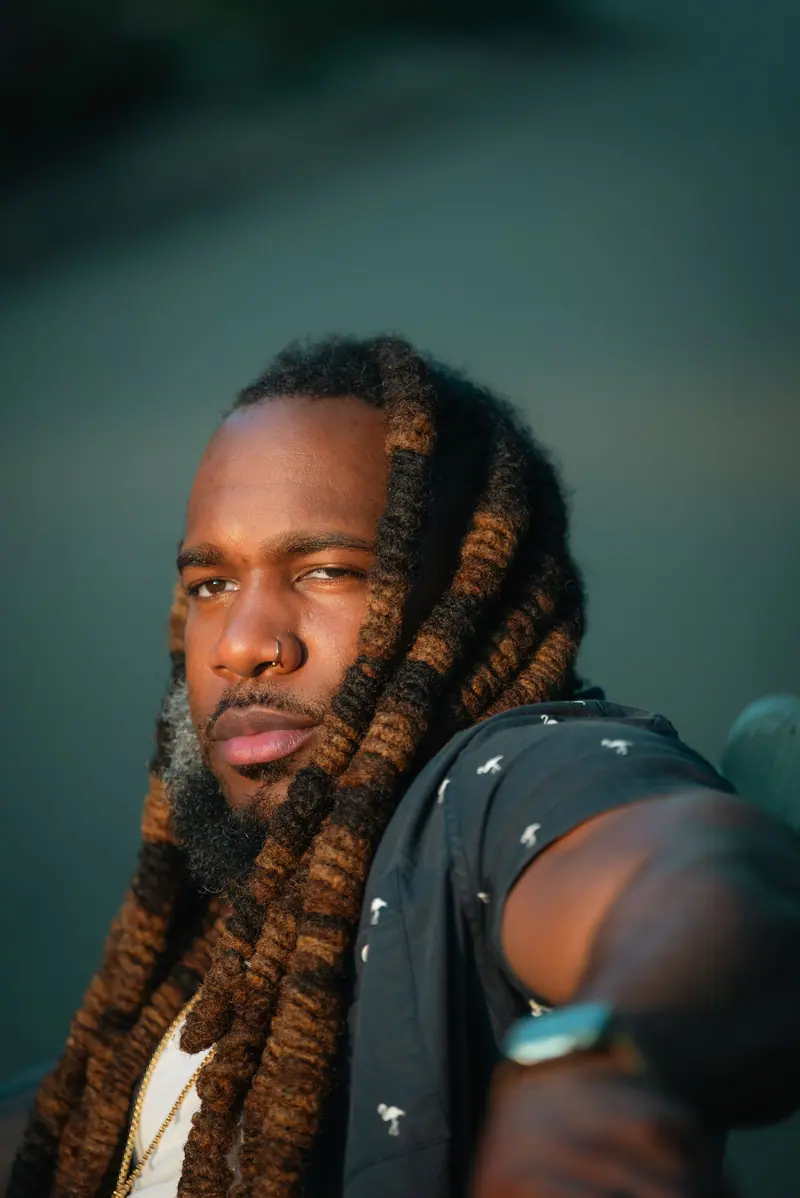 Stylish man with dreadlocks and nose piercing in warm sunlight. Outdoor portrait.