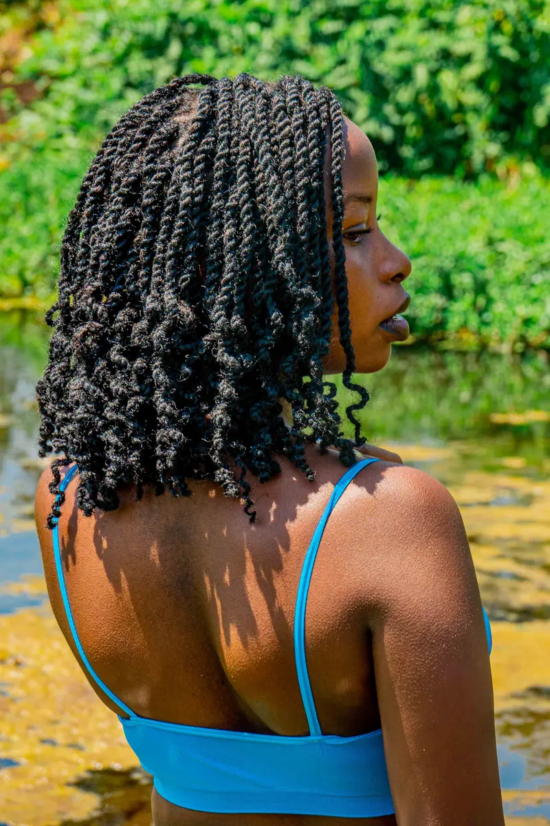 Portrait of a young woman with braided hairstyle in a bright blue tank top by a natural setting.