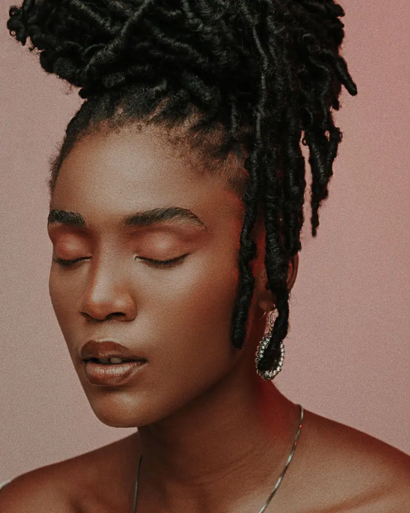 Serene portrait of a woman with closed eyes and stylish dreadlocks against a soft background.