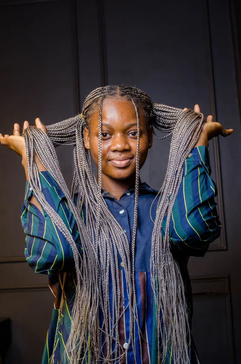 A joyful woman poses with braided hair in an indoor setting.