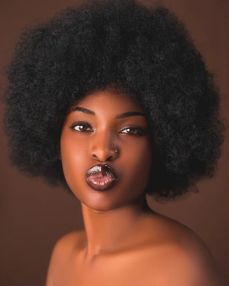 A captivating studio portrait of a young woman with an afro hairstyle, showcasing elegance and style.