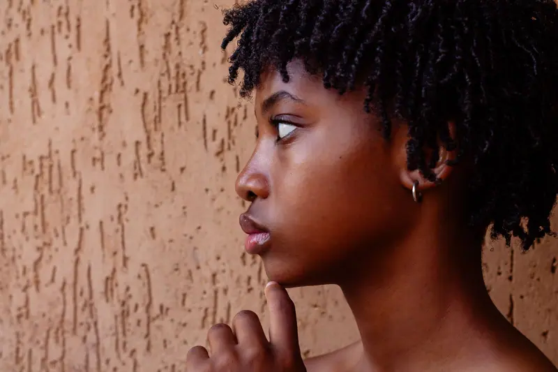 A thoughtful side profile portrait of a young woman with curly hair against a textured wall.