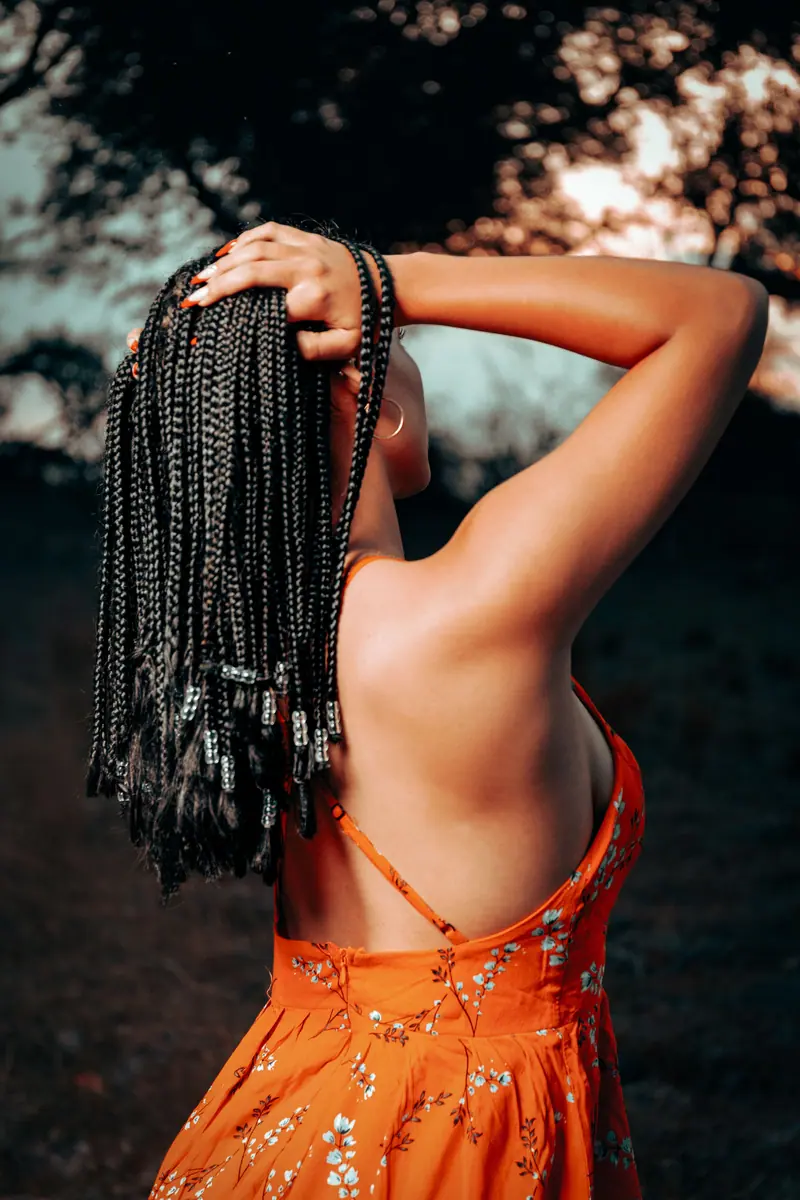Back view of a woman with braided hair enjoying a sunset outdoors in a bright orange summer dress.