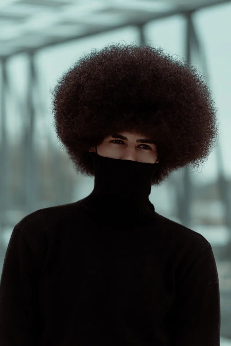 A fashionable man with an afro hairstyle wearing a turtleneck sweater, posing outdoors.
