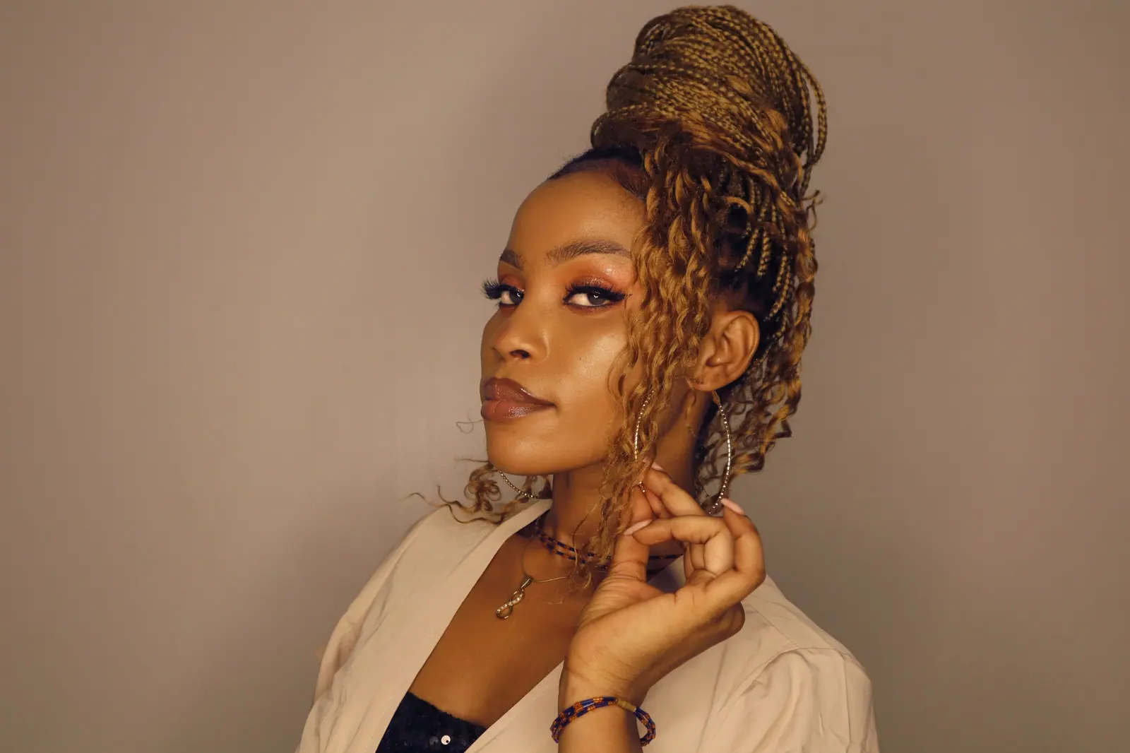 Woman with honey-gold goddess braids swept into a high bun against a warm taupe wall