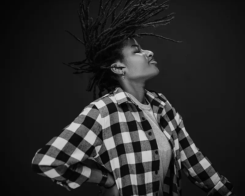 Striking black and white portrait of a woman with dreadlocks, wearing a plaid shirt, captured in motion.