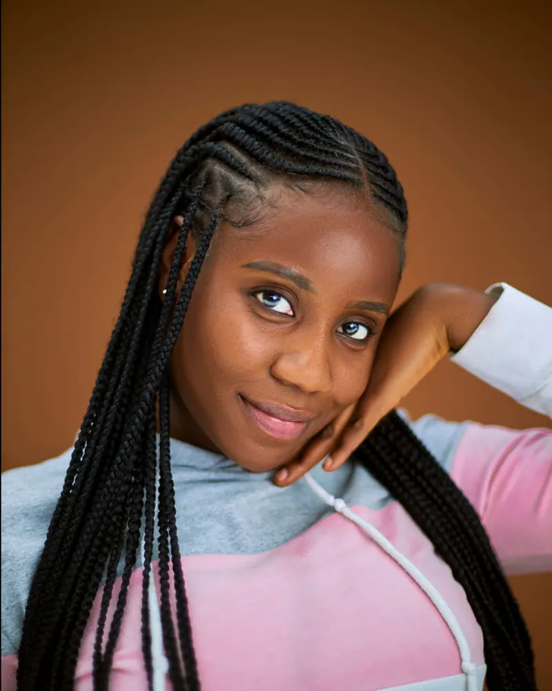 Portrait of a woman with braided hair smiling against a brown background, exuding warmth and style.