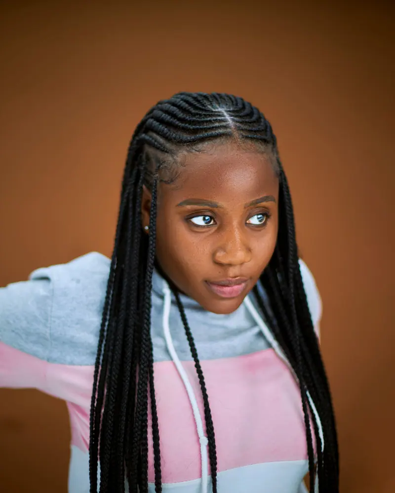 Stylish portrait of a young woman with braided hair, posing casually indoors.