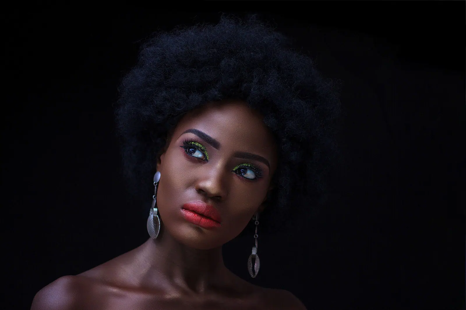 Woman with a full natural afro, ruby lips and pearl earrings against black