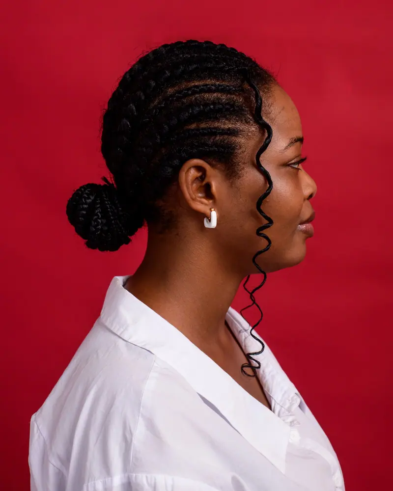 Striking studio portrait of a woman with braided hair, posing against a bold red background.