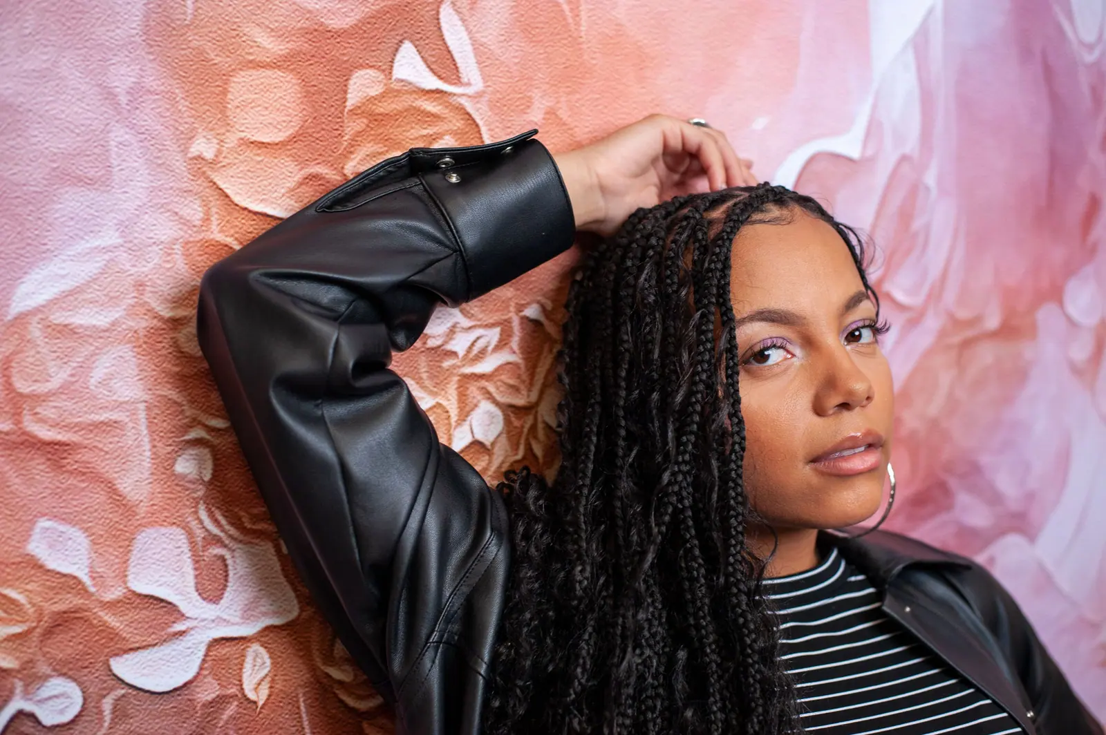 Woman with long faux locs posing against a hand-painted blush floral wall