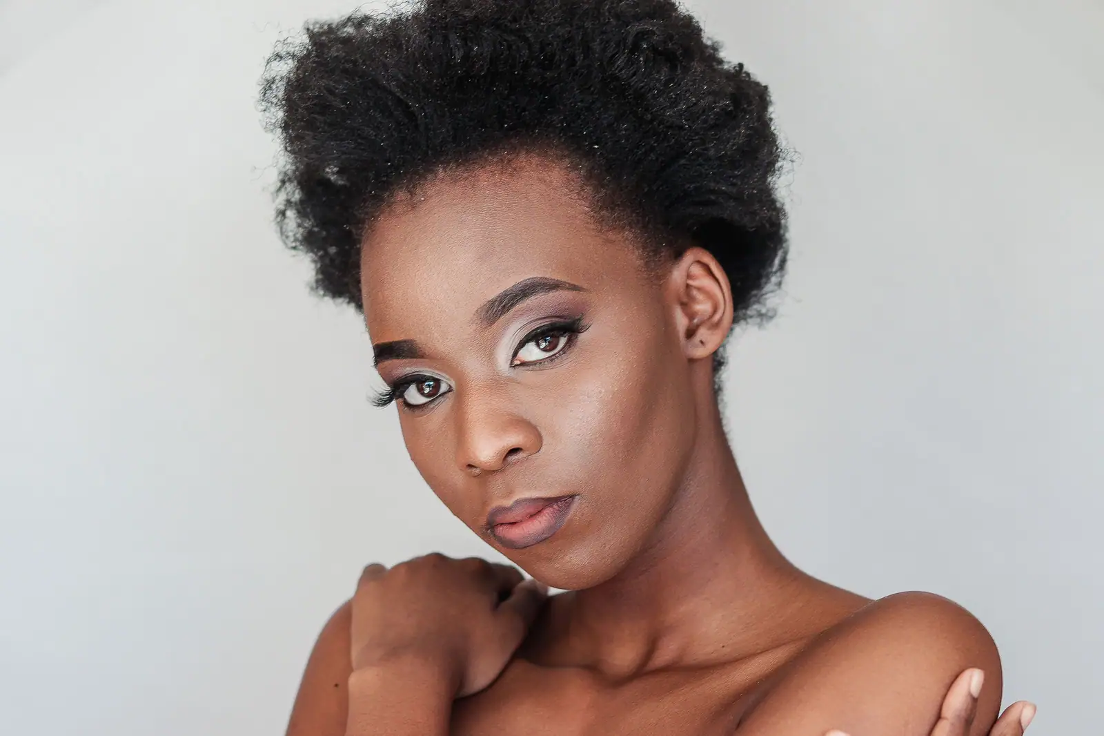 Elegant studio portrait of a young woman with natural afro hair and artistic makeup.