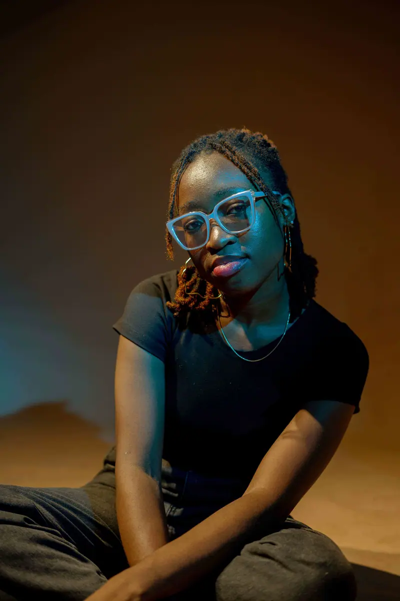 Stylish woman with locs and glasses, captured in a warm, artistic setting for fashion and lifestyle.