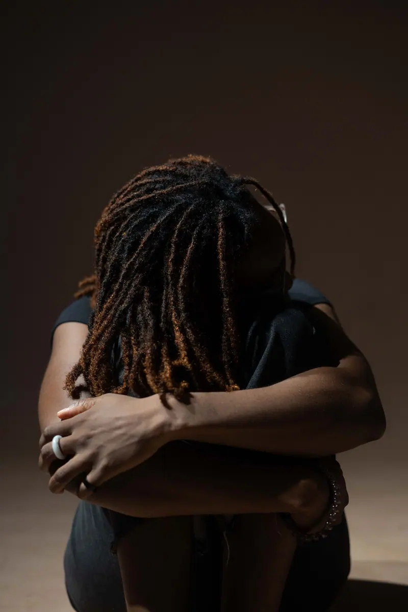 Artistic portrait of a woman hugging knees, dreadlocks styled, dramatic lighting.