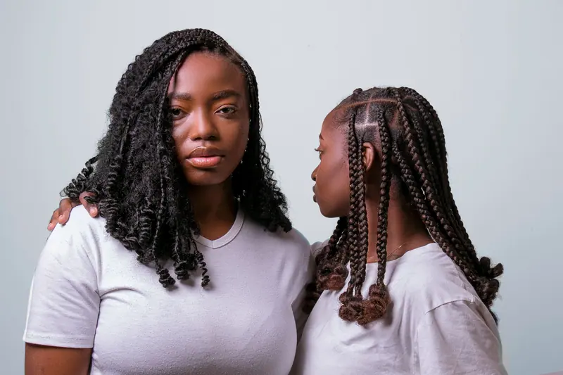 Close-up of two women with braided hairstyles in a warm and intimate portrait setting.