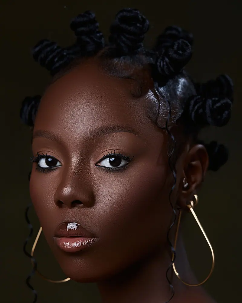 Elegant portrait of a woman with Bantu knots and gold earrings against a dark background.