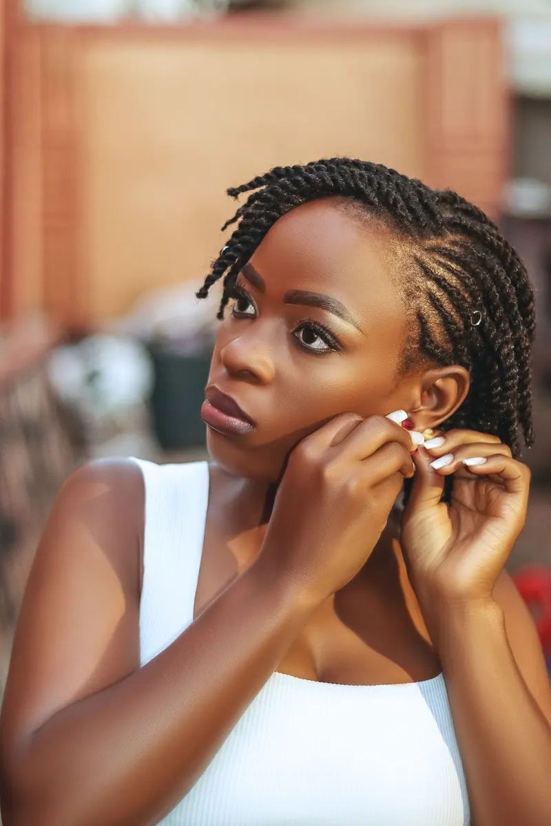 A stylish young woman adjusting her earrings with focus, captured in natural light.