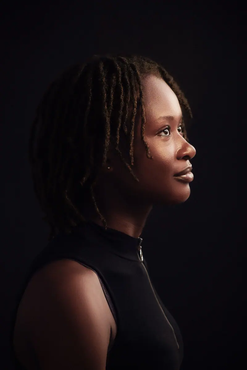 Artistic side profile portrait of a woman with dreadlocks against a dark background.
