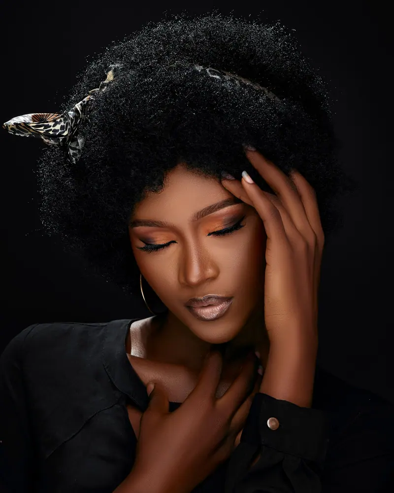 Stunning portrait of a woman with afro hairstyle and subtle makeup, in striking black attire.