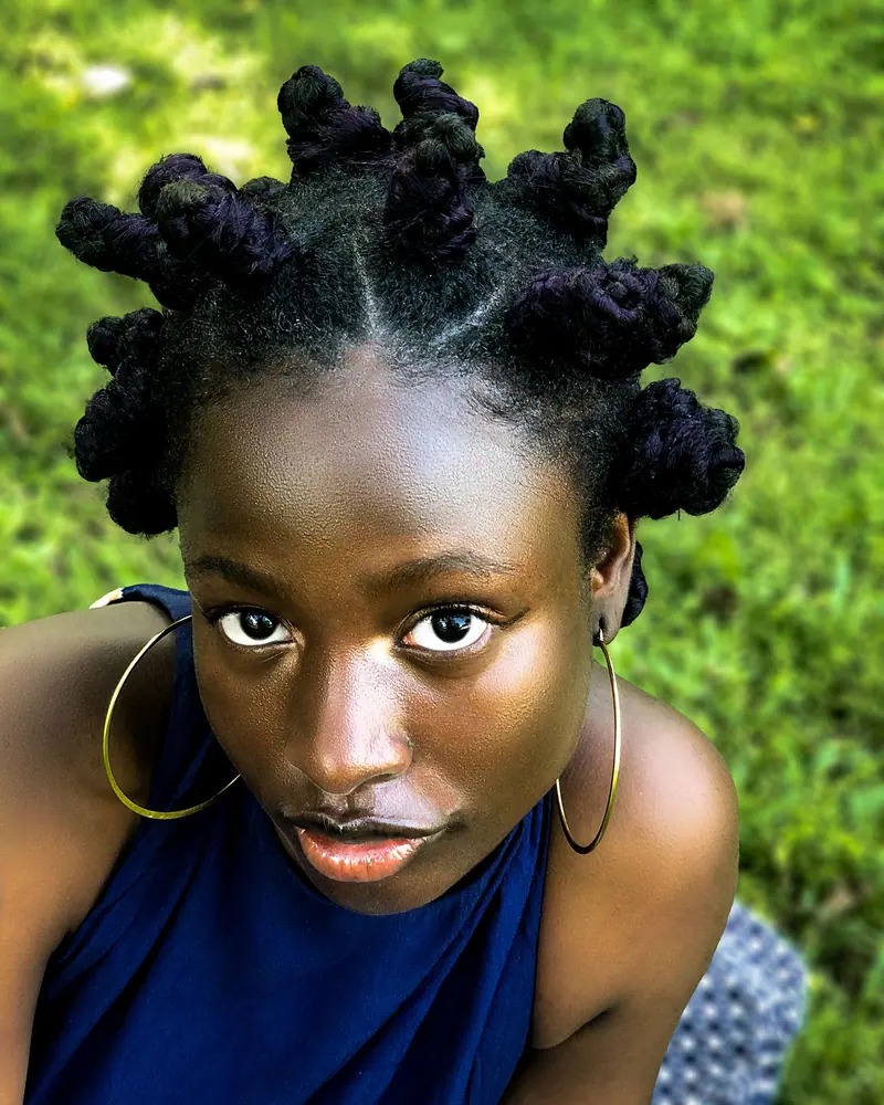 A youthful portrait featuring a woman with Bantu knots enjoying the outdoors, exuding confidence and style.