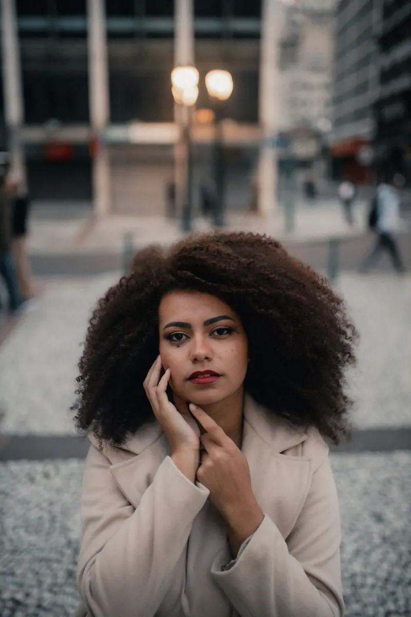 Portrait of a woman with curly hair in an urban environment during dusk with soft lighting.
